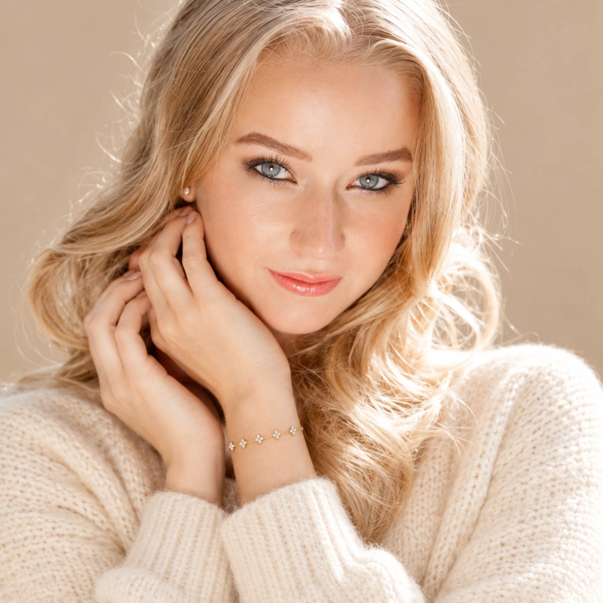 Blonde model in a cream knit sweater wearing the gold tone Clover Zircon Station Bracelet