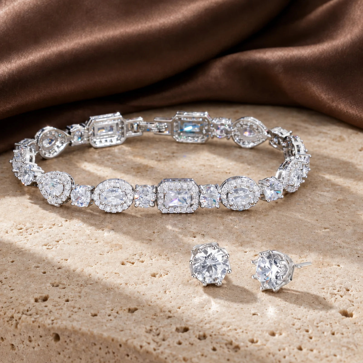 Zircon Glow Set in silver tone: tennis bracelet with emerald, oval and pear cubic zirconia halos and round stud earrings on beige travertine with brown satin